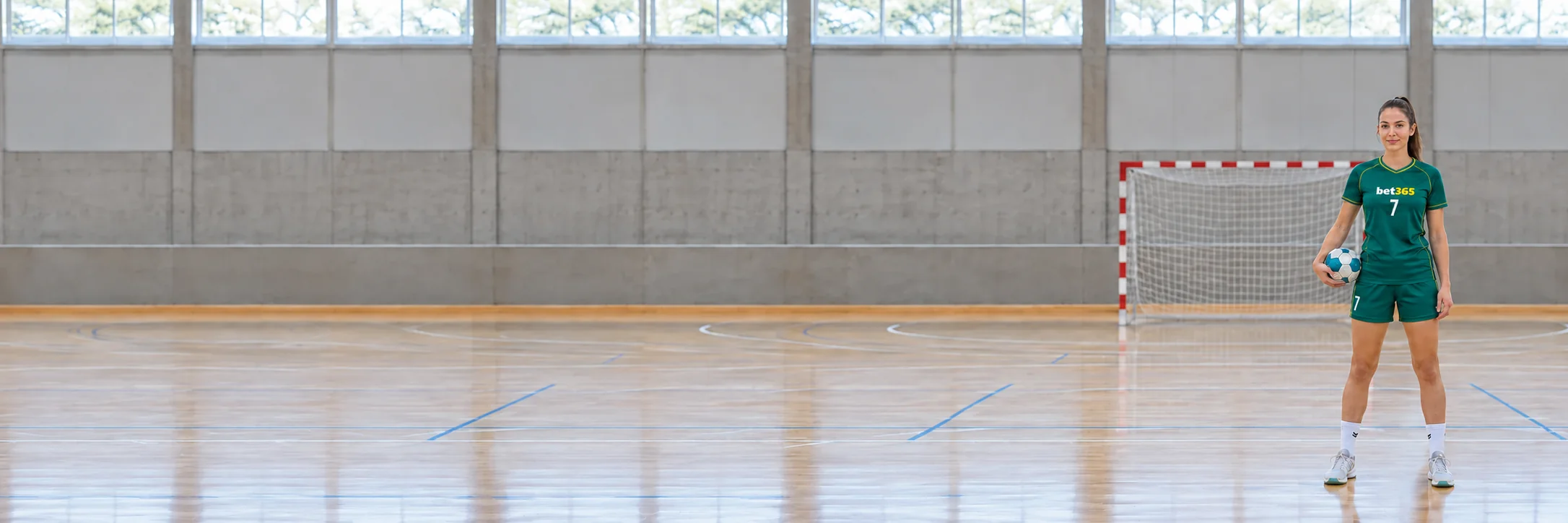 Fictional adult handball player beside a goal on an indoor court in bet365 colours